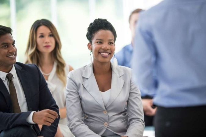 Une participante souriante en costume gris écoute attentivement un intervenant durant une formation CSE en entreprise.