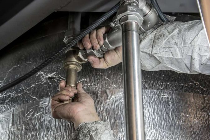 Un technicien intervient sur des canalisations en plomb et des raccords métalliques dans un espace technique.