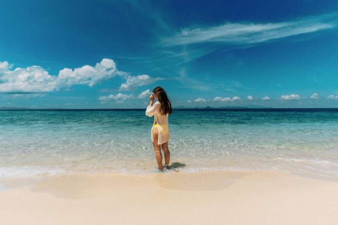 Une femme debout dans l'eau cristalline d'une plage de sable fin, face à l'horizon marin lors d'un séjour à la plage.